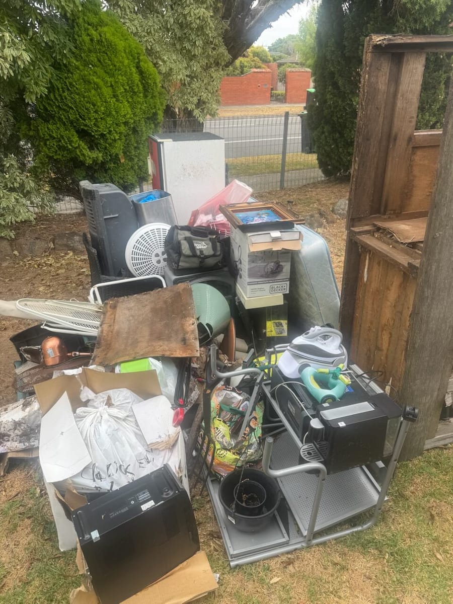 Backyard junk pile beside a fence before household rubbish removal in Melbourne
