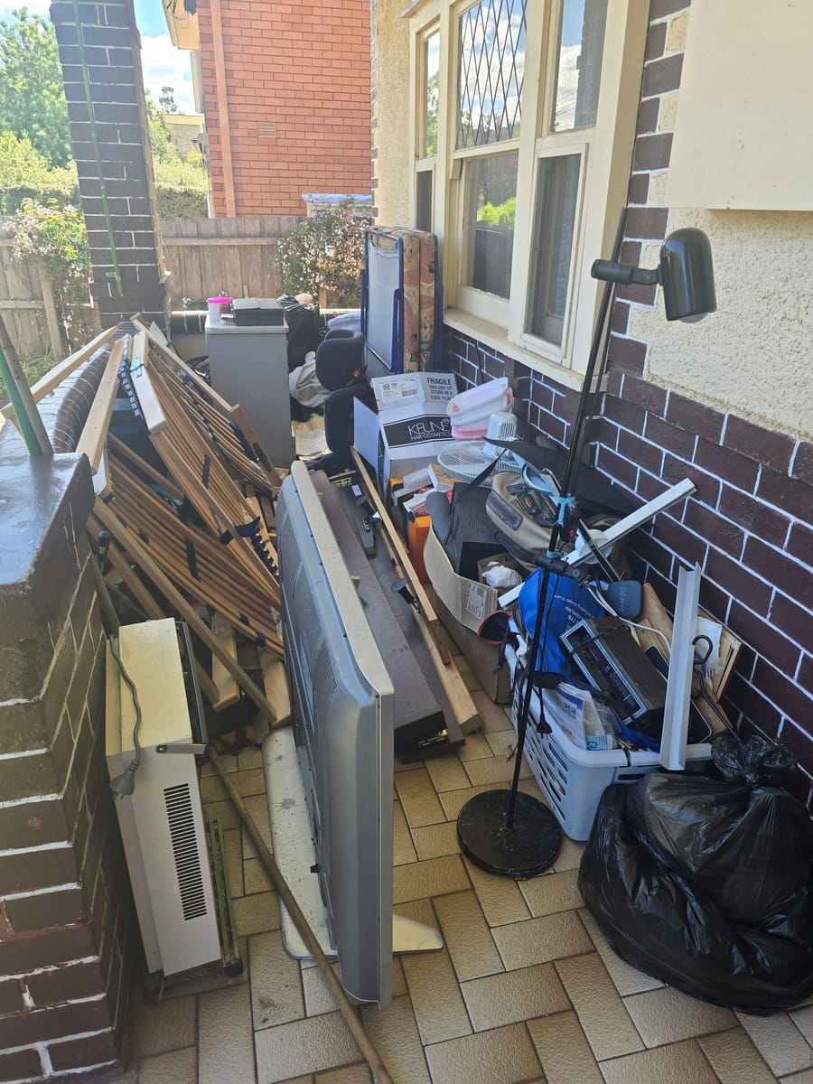 Tiled verandah cluttered with old window frames and junk before rubbish removal in Melbourne